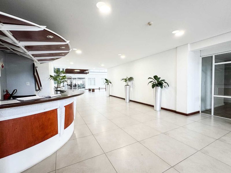 Spacious commercial entrance lobby featuring a built-in reception desk, neutral tiled flooring, and recessed lighting, creating a clean and professional welcome area.