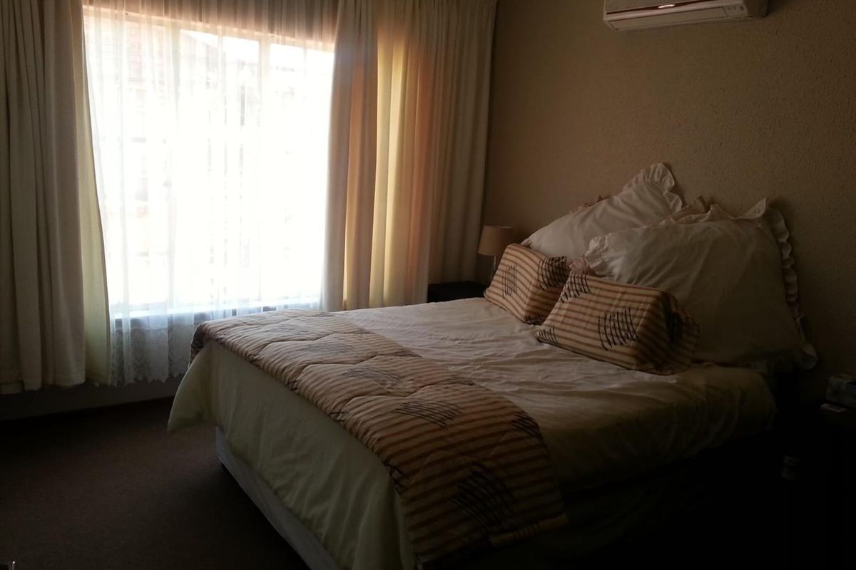 A bedroom featuring a wall-mounted air conditioning unit and large window with curtains, providing natural light.