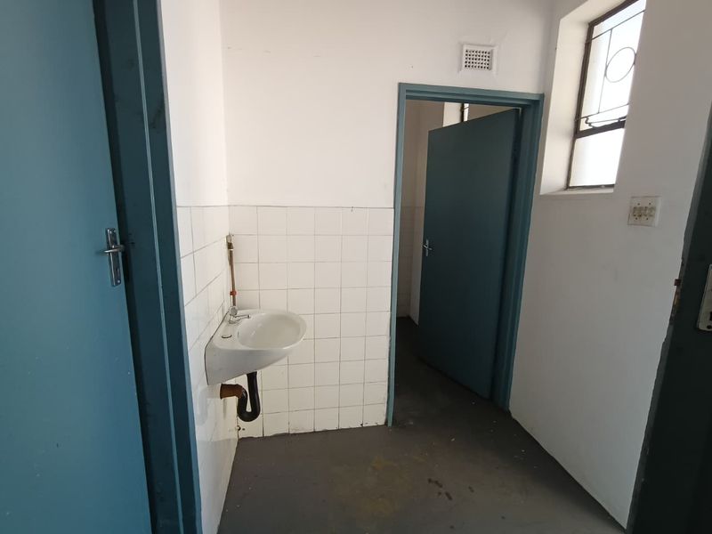A functional utility space featuring a wall-mounted basin with tiled splashback, leaded glass window, and direct access to adjacent rooms.