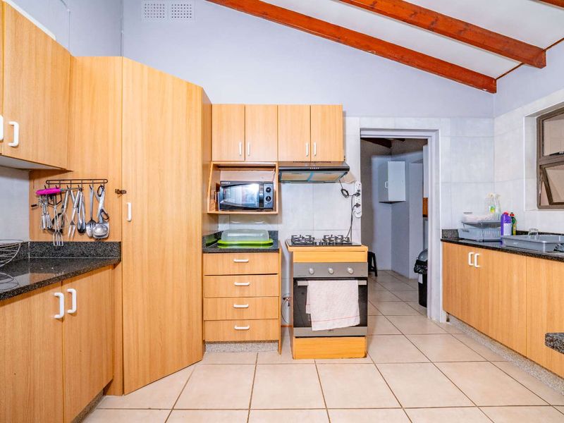 A functional kitchen featuring laminate cabinetry, granite countertops, a gas stove with extractor, and exposed timber ceiling beams, leading to a secondary utility area.