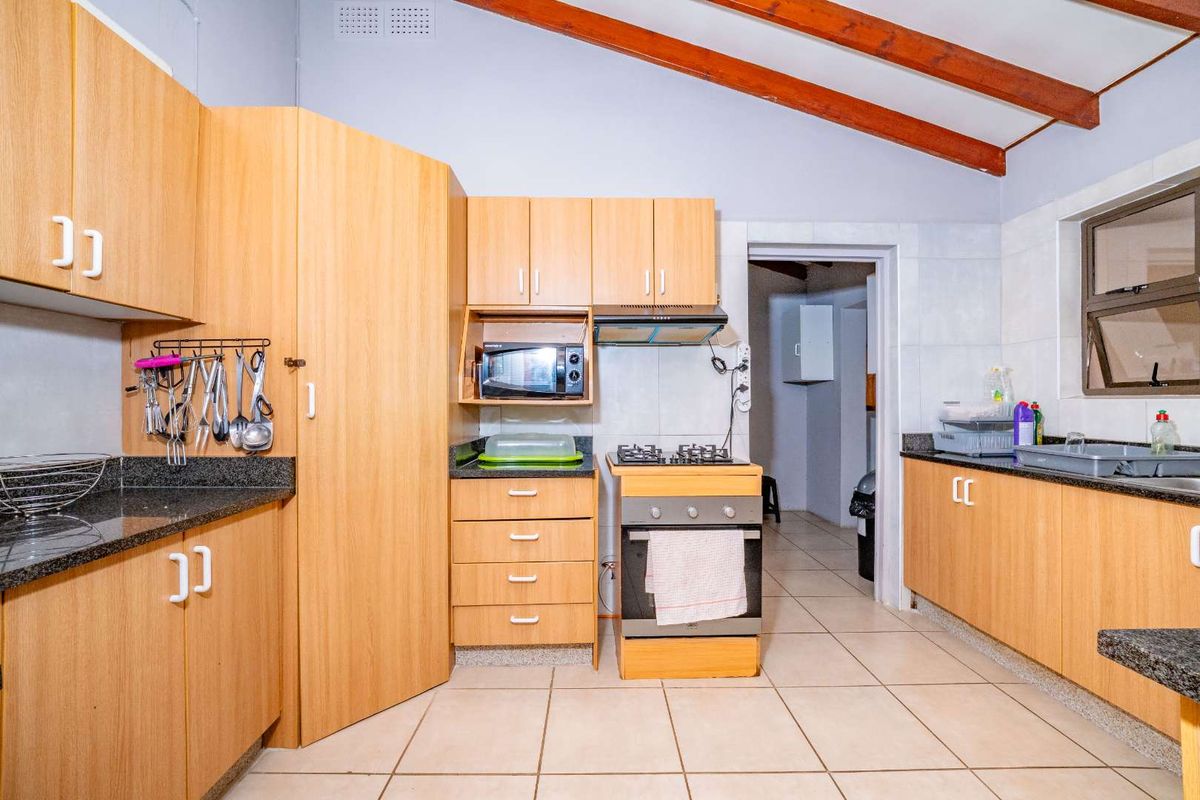 A functional kitchen featuring laminate cabinetry, granite countertops, a gas stove with extractor, and exposed timber ceiling beams, leading to a secondary utility area.