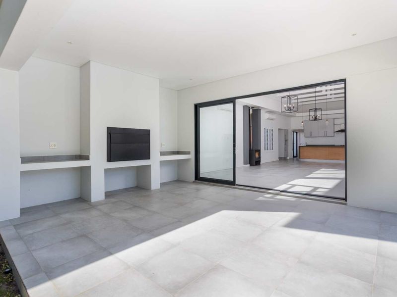 A spacious covered patio featuring a built-in braai, concrete prep counters, and large sliding doors providing seamless access to the open-plan interior living area.