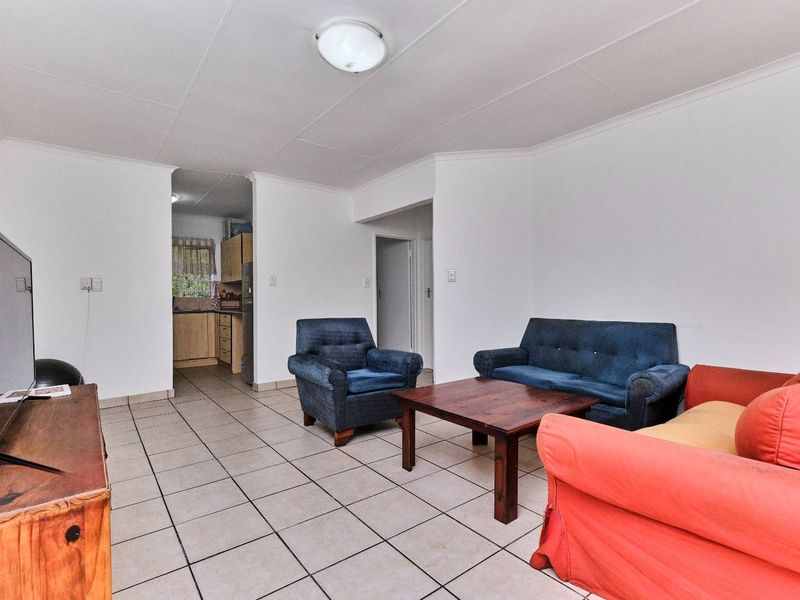 Open plan living area with tiled flooring, leading into a functional kitchen space with built-in cabinetry.