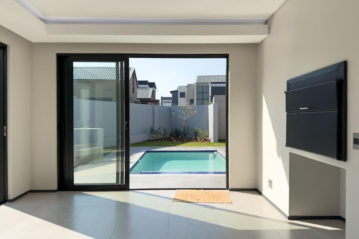 Modern living area featuring large sliding doors opening to a private pool and garden, complete with a built-in braai and neutral tiled flooring.