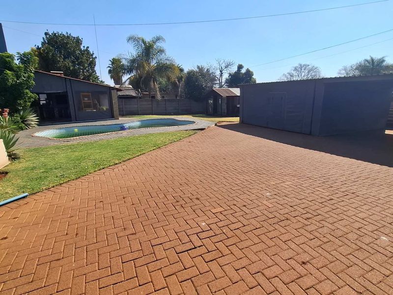 Spacious rear exterior featuring a paved courtyard, swimming pool, and a detached outbuilding, providing ample outdoor space and utility.