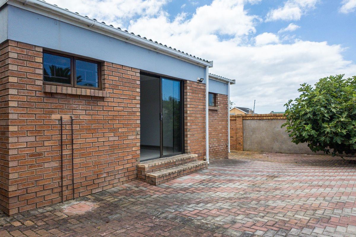 Rear view of the townhouse featuring a brick facade, sliding glass door access, and a paved courtyard area.