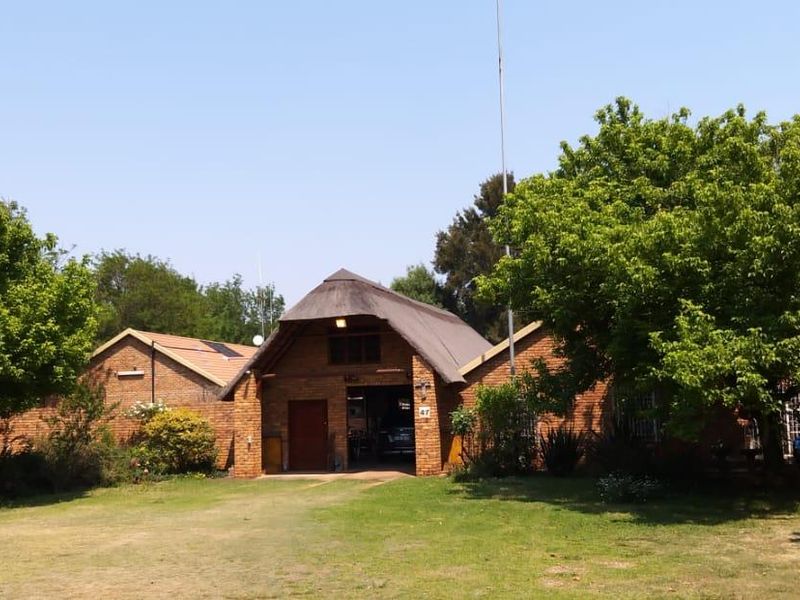 Front view of a facebrick small holding property featuring a traditional thatch roof design and established garden surroundings.