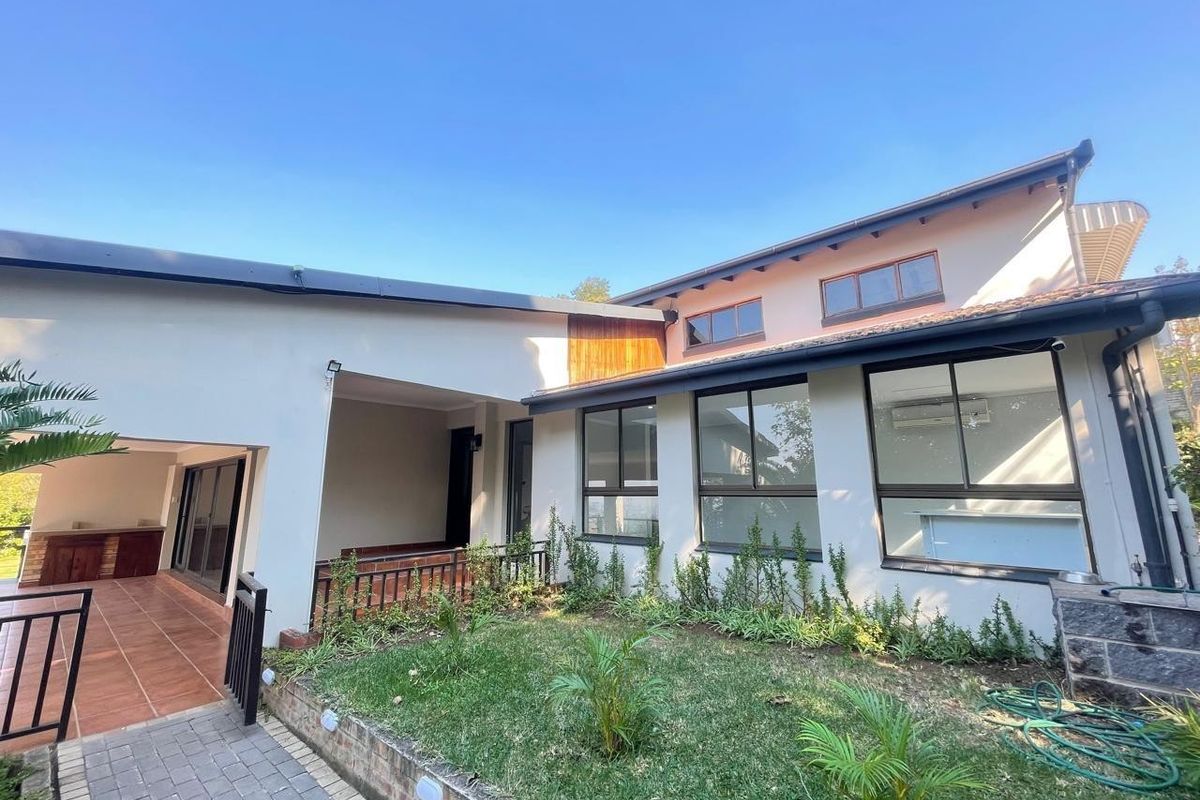 Rear view of the property featuring a covered tiled patio, landscaped garden with a brick retaining wall, and modern aluminum-framed windows.
