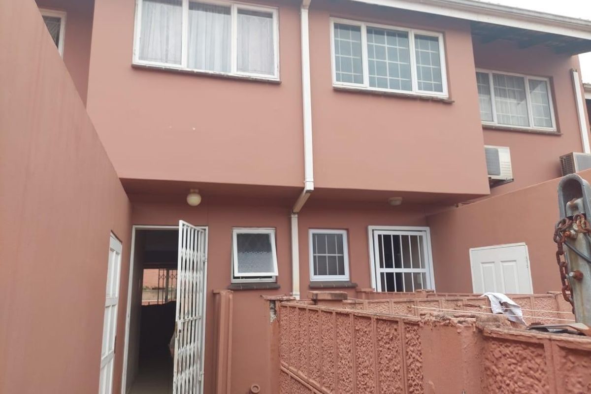 Rear exterior view of the apartment building featuring a private entrance, security gate, and multiple windows with a paved courtyard area.