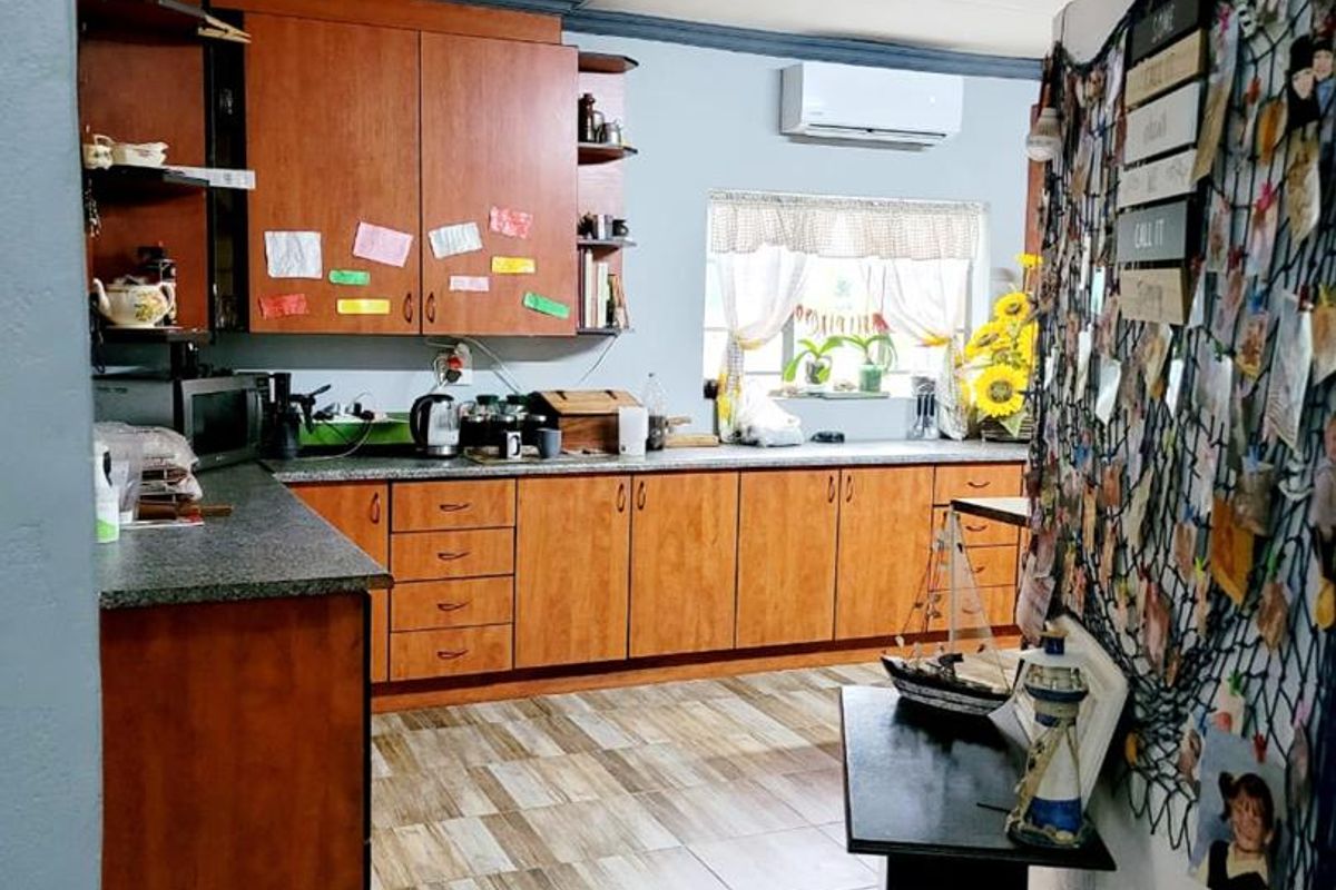 A functional kitchen featuring wood-veneer cabinetry, stone-look countertops, tiled flooring, and a wall-mounted air conditioning unit.