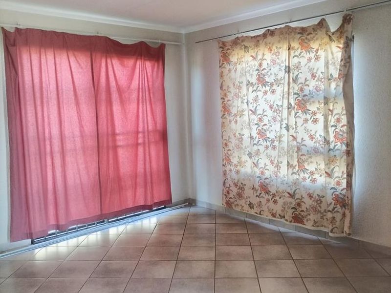 An empty living area featuring neutral ceramic floor tiles and dual window treatments with installed curtain tracks.