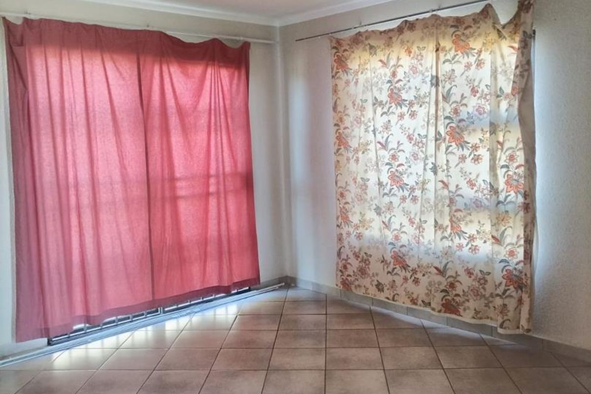 An empty living area featuring neutral ceramic floor tiles and dual window treatments with installed curtain tracks.