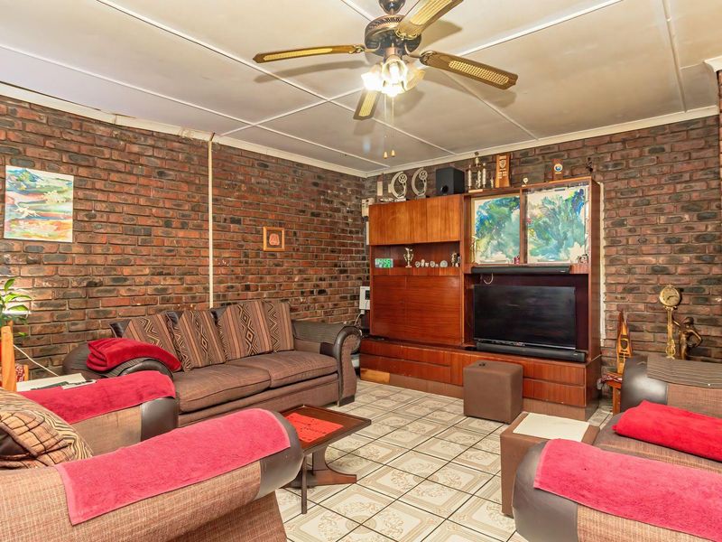 Living room featuring exposed brick walls, ceramic floor tiles, and a ceiling fan.