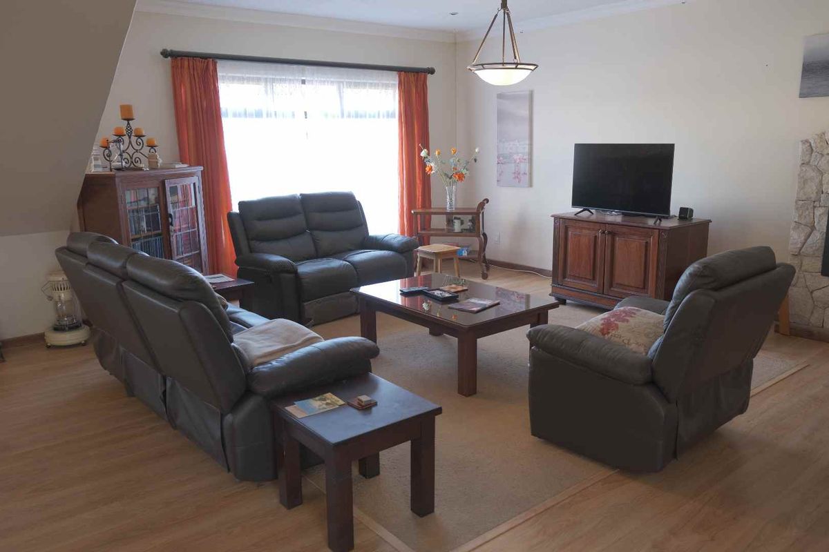 A spacious living room featuring light wood-look flooring, a stone-clad fireplace feature, and a large window with natural light.