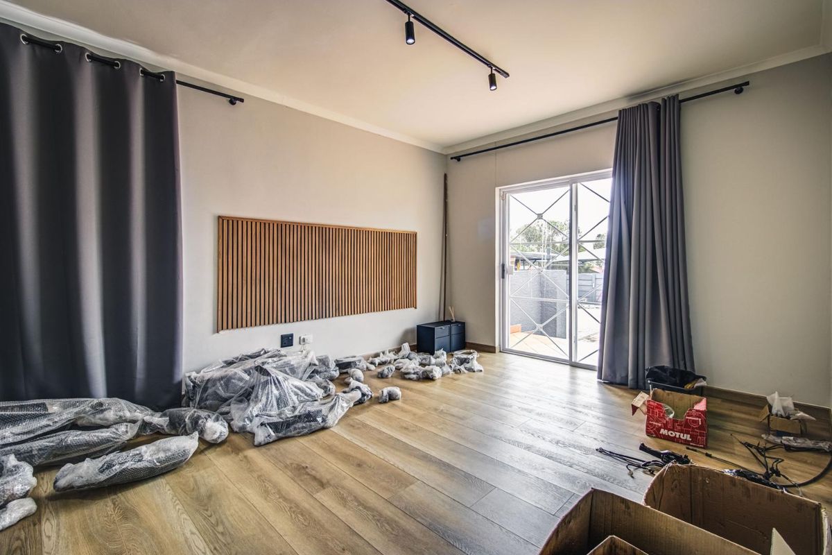 A bright living room featuring light wood-look flooring, a decorative timber slat wall panel, track lighting, and a sliding glass door leading to the exterior.