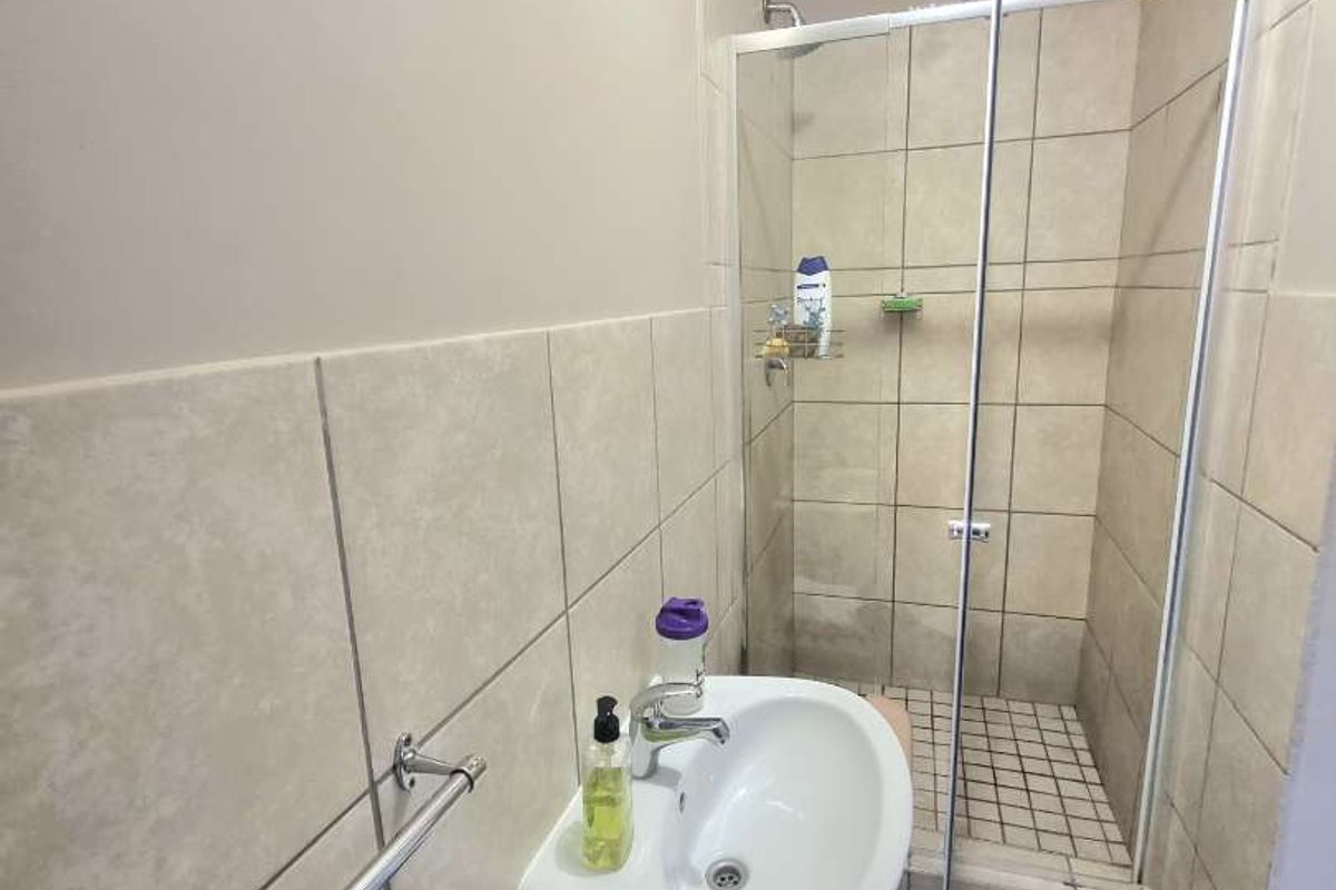 A functional bathroom featuring a wall-mounted basin, a tiled shower enclosure with a glass door, and neutral ceramic wall and floor tiling.