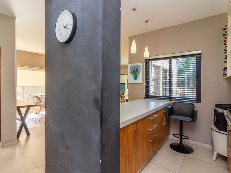 A modern kitchen area featuring wood-veneer cabinetry, stone countertops, and pendant lighting, with an open-plan layout connecting to the adjacent dining space.