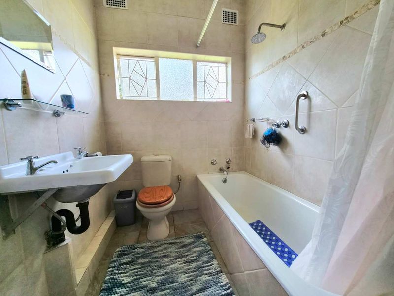 A functional bathroom featuring a wall-mounted basin, toilet, and a combined bathtub and shower setup with tiled finishes.