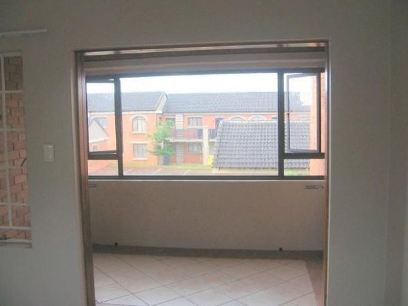 An empty, covered balcony area featuring tiled flooring and aluminium-framed windows, offering a view of the surrounding townhouse complex.