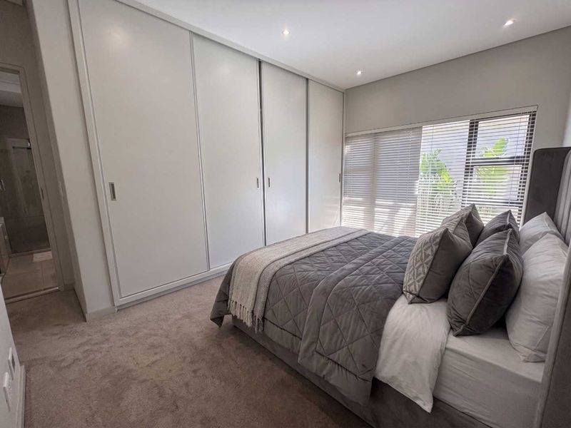 A modern bedroom featuring neutral carpet flooring, recessed downlights, venetian blinds, and a large built-in sliding door wardrobe.