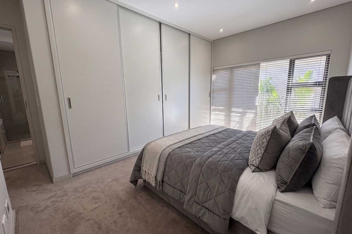 A modern bedroom featuring neutral carpet flooring, recessed downlights, venetian blinds, and a large built-in sliding door wardrobe.