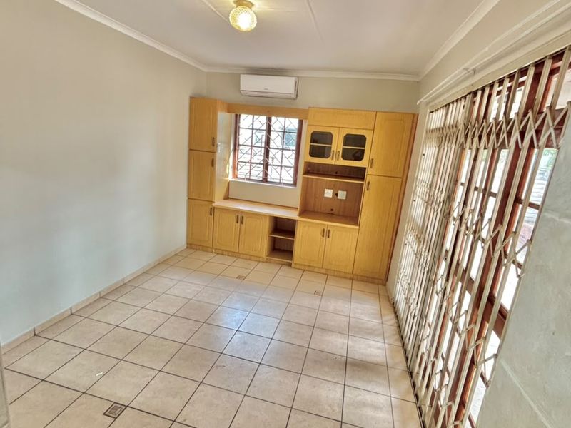 An empty living area featuring tiled flooring, built-in wooden cabinetry, an air conditioning unit, and a secure sliding door with a metal security gate.