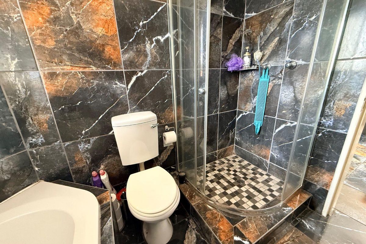 A compact bathroom featuring dark marble-effect wall and floor tiles, a corner glass shower enclosure, and a standard white toilet.