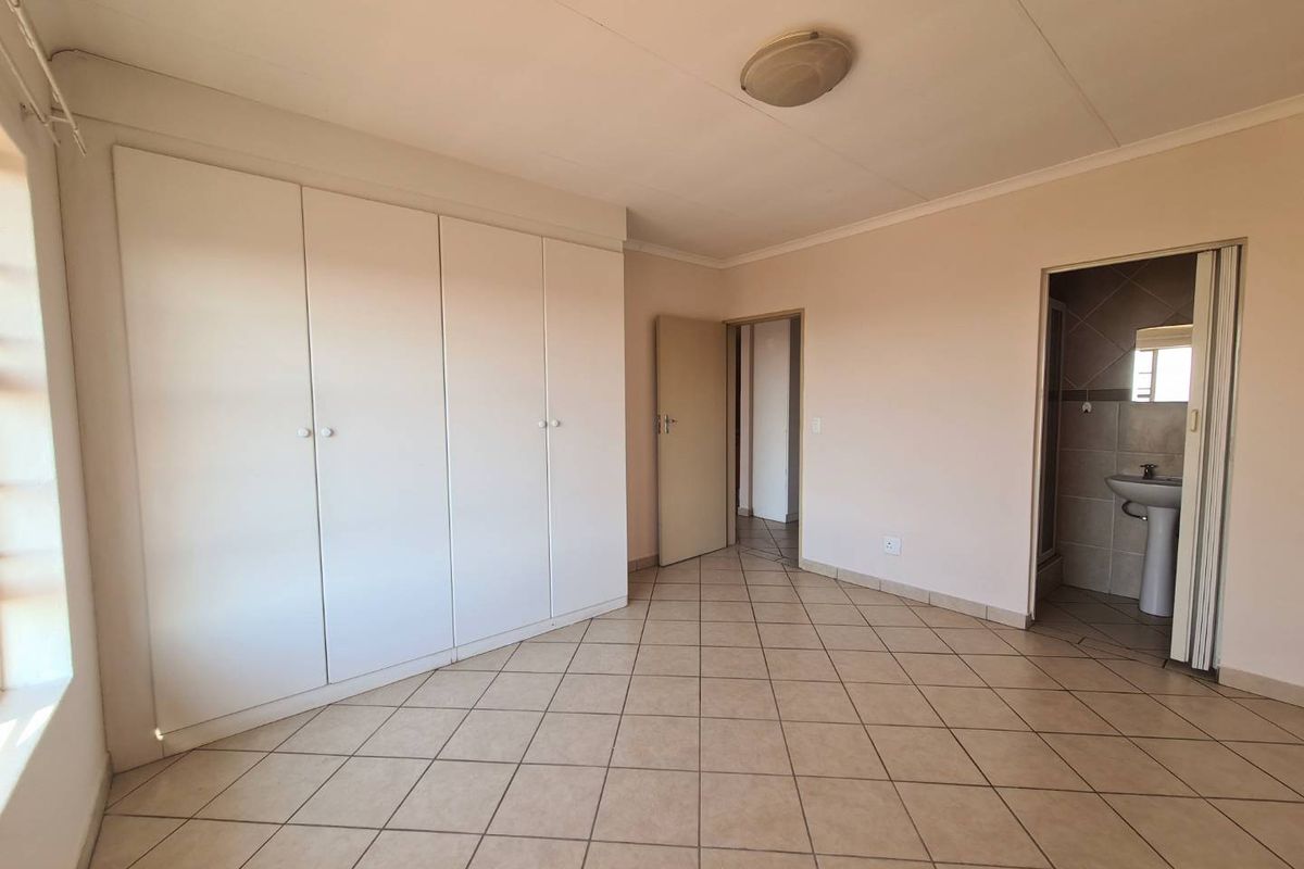 A spacious, empty bedroom featuring neutral tiled flooring, ample built-in cupboard storage, and direct access to an en-suite bathroom.
