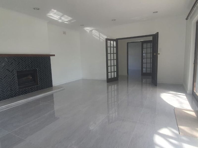 Spacious living room featuring polished tiled floors, a modern herringbone-tiled fireplace with a timber mantel, and large sliding glass doors leading outdoors.