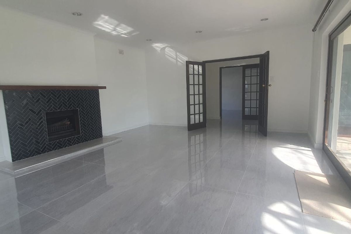 Spacious living room featuring polished tiled floors, a modern herringbone-tiled fireplace with a timber mantel, and large sliding glass doors leading outdoors.