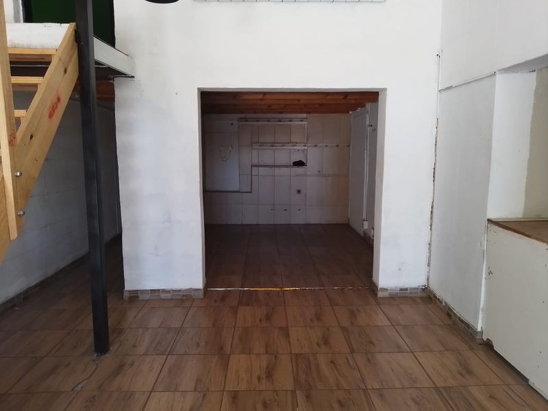 An open-plan retail space featuring wood-look tiled flooring, a wooden staircase, and a recessed area with built-in shelving and exposed timber ceiling beams.