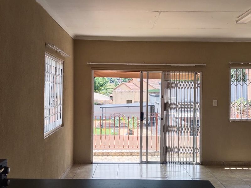 An empty living room featuring tiled floors, security gates on the sliding door, and burglar bars on the windows, offering a blank canvas for renovation.