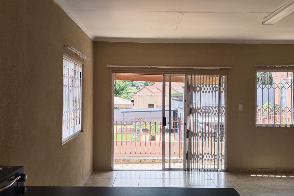 An empty living room featuring tiled floors, security gates on the sliding door, and burglar bars on the windows, offering a blank canvas for renovation.