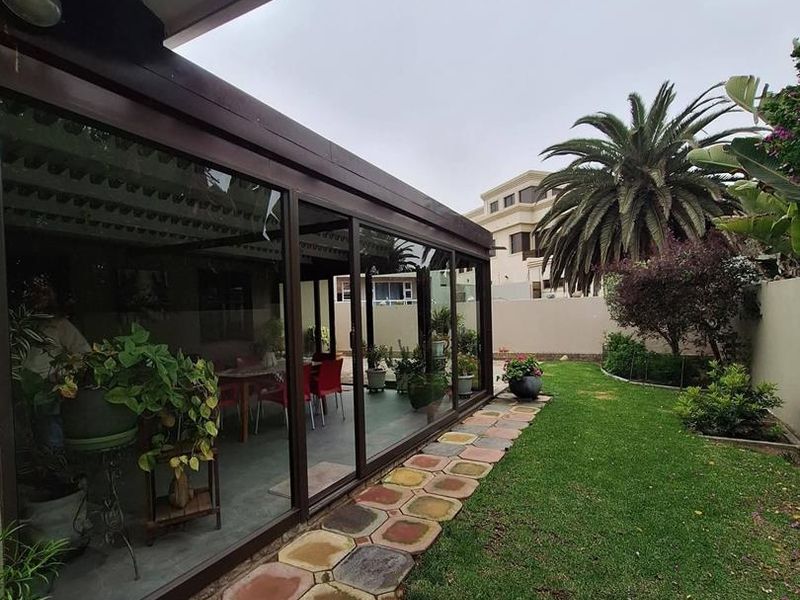 Rear garden view featuring an enclosed patio with sliding glass doors, a paved walkway, and a well-maintained lawn area.