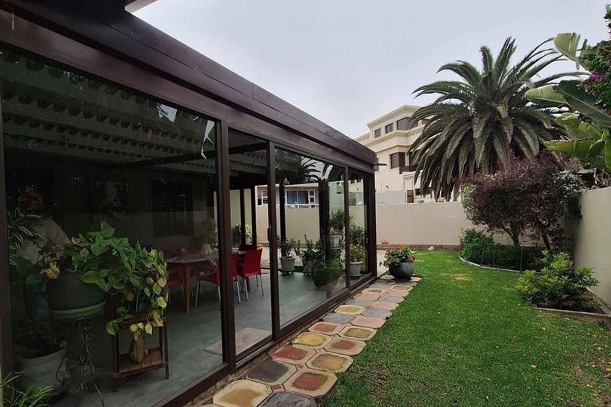 Rear garden view featuring an enclosed patio with sliding glass doors, a paved walkway, and a well-maintained lawn area.