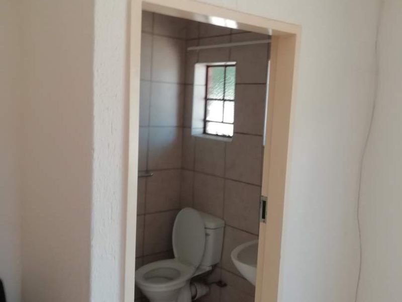 A compact bathroom featuring a toilet and washbasin with tiled walls and flooring, accessible via a doorway.