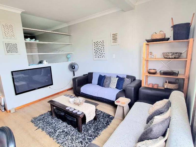 A comfortable living room featuring laminate flooring, built-in wall shelving, and a central pendant light fixture.