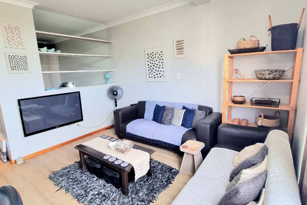 A comfortable living room featuring laminate flooring, built-in wall shelving, and a central pendant light fixture.
