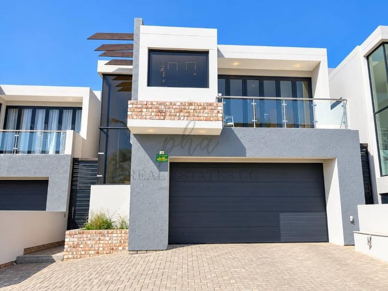 Modern townhouse exterior featuring a double garage, paved driveway, and an upper-level balcony with glass balustrades and contemporary architectural finishes.