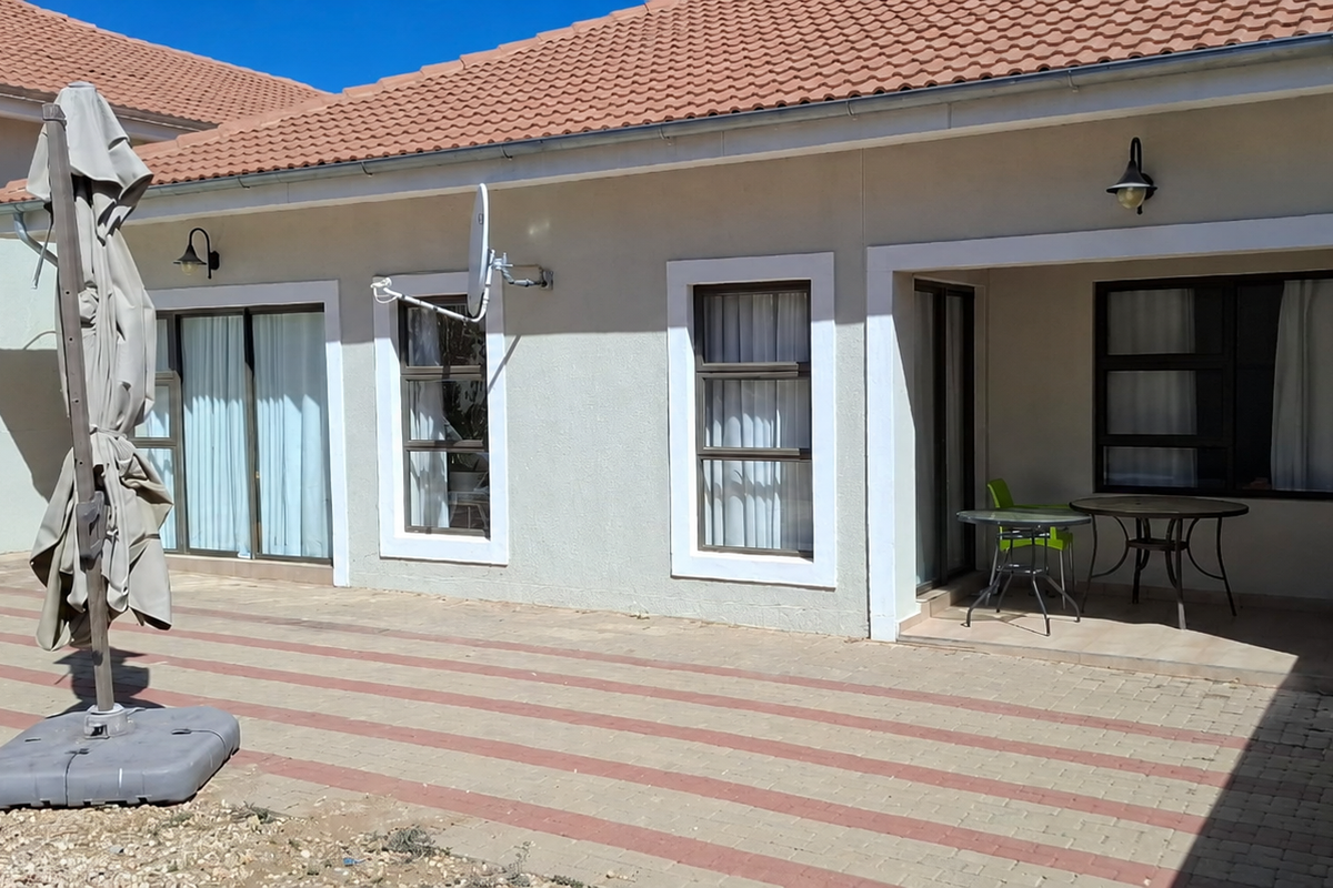 Rear exterior view of the townhouse featuring a paved patio area, sliding glass doors, and low-maintenance tiled roof construction.