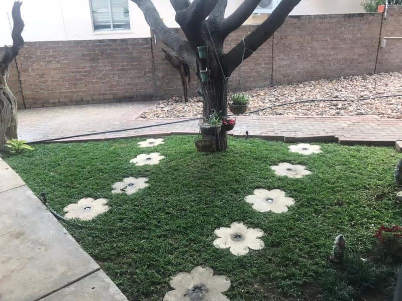 A private garden area featuring a mature tree, decorative flower-shaped stepping stones, paved pathways, and a brick boundary wall.