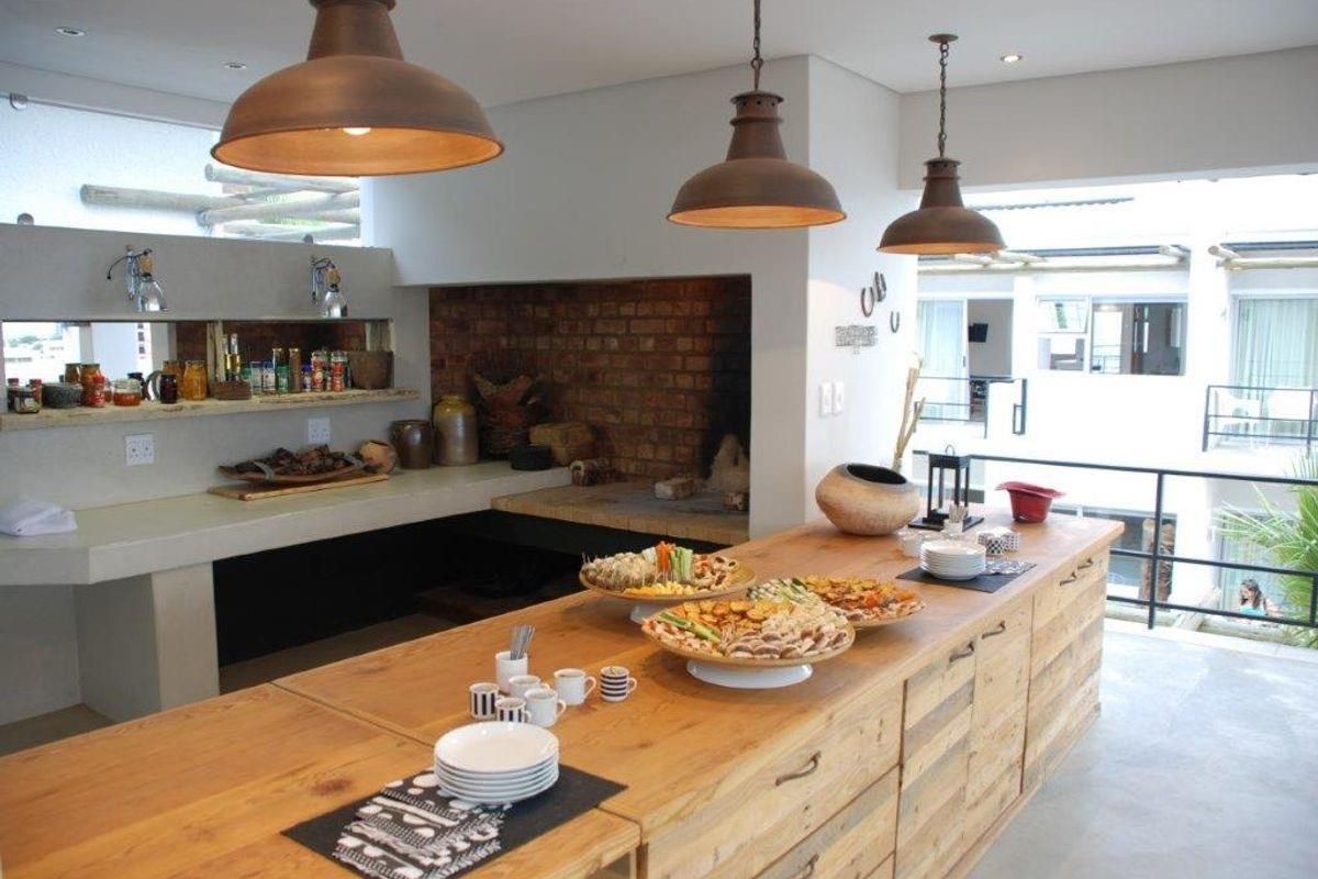 Spacious kitchen area featuring a large built-in brick fireplace, concrete countertops, and industrial-style pendant lighting, creating a warm and functional cooking and entertainment space.