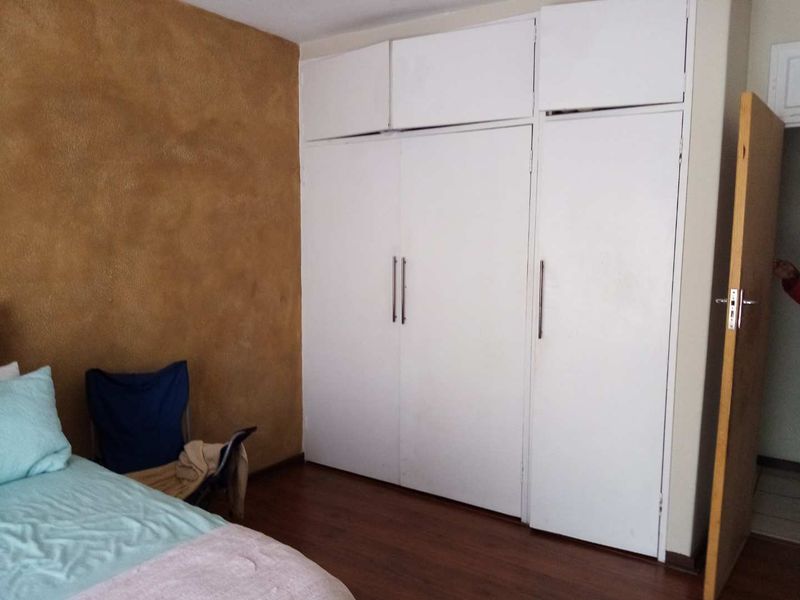 Bedroom featuring laminate flooring and white built-in cupboards with overhead storage compartments.
