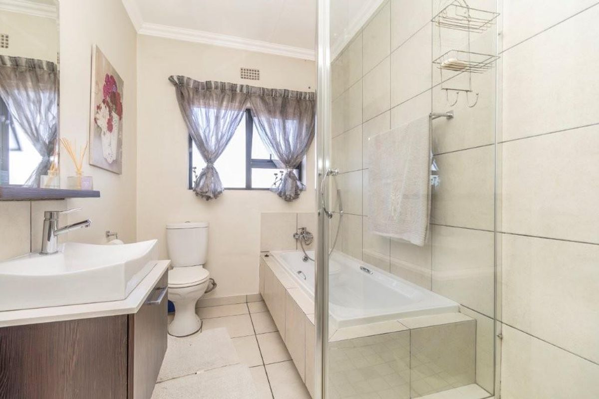 A well-maintained bathroom featuring a vanity with a vessel sink, a toilet, and a combined bathtub and glass-enclosed shower area with neutral tiling.