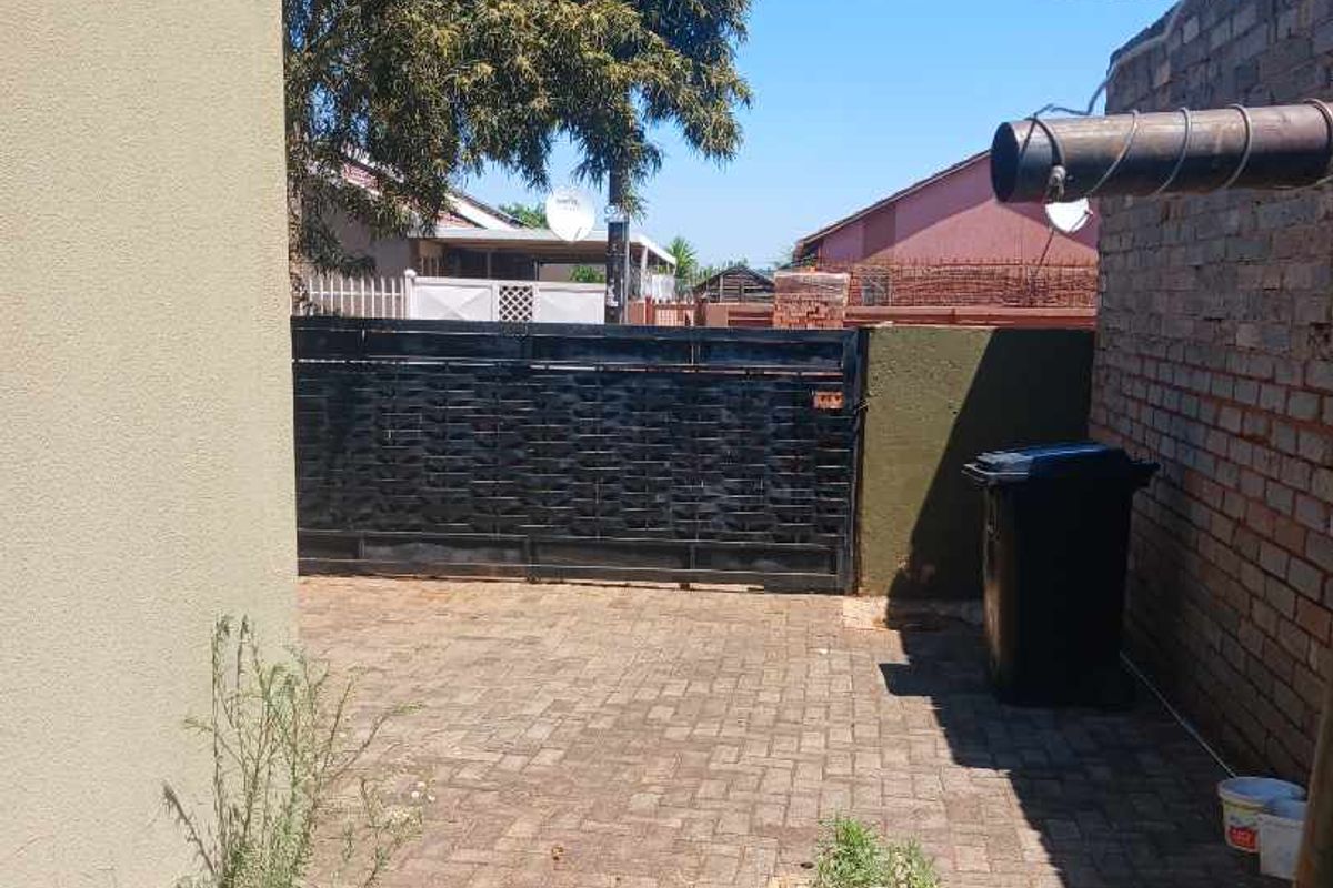 A paved rear courtyard area featuring a brick boundary wall and a metal sliding gate, providing a functional outdoor space.