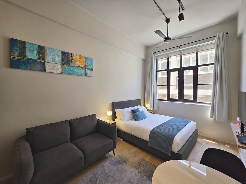 A well-maintained bedroom featuring laminate flooring, a ceiling fan, and a large multi-pane window that provides natural light.