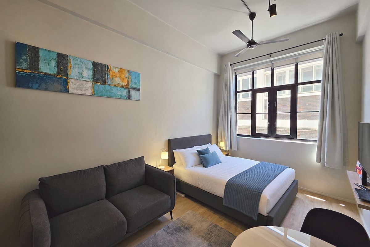 A well-maintained bedroom featuring laminate flooring, a ceiling fan, and a large multi-pane window that provides natural light.