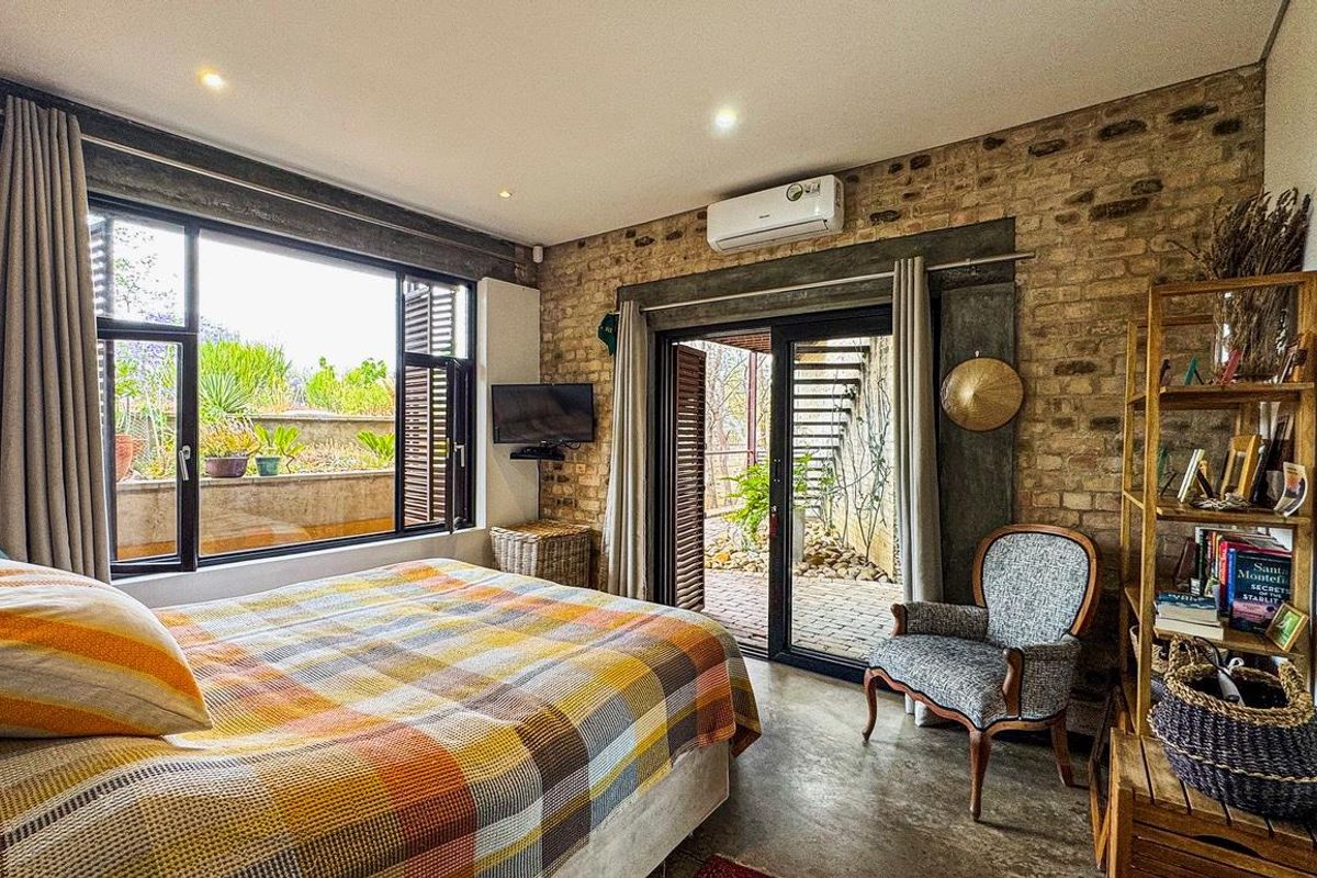 A bedroom featuring exposed brick walls, polished concrete flooring, and direct access to an outdoor patio through sliding glass doors.