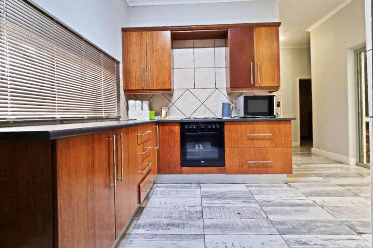 A functional kitchen featuring wood-veneer cabinetry, built-in oven, hob, and tiled flooring with a neutral backsplash.