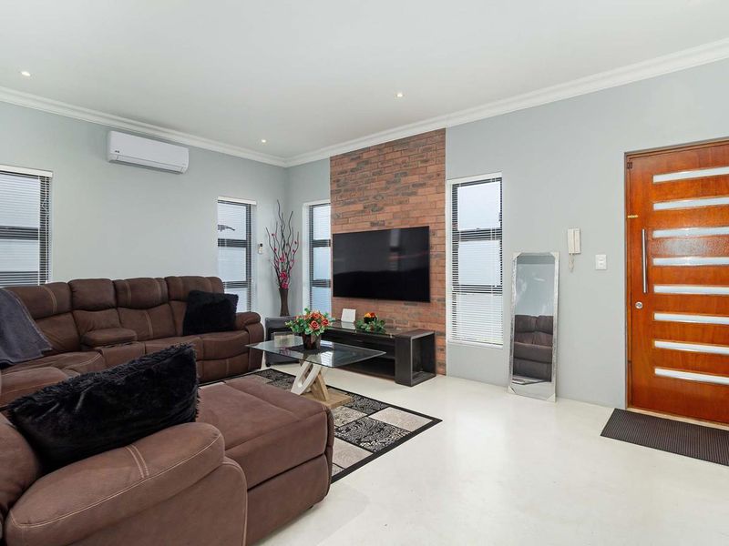 Spacious living room featuring an exposed brick feature wall, split-system air conditioning, recessed lighting, and a solid timber front entrance door.